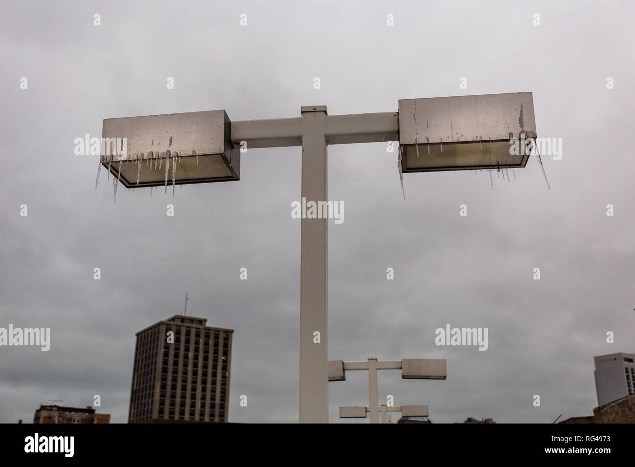 Gefrorenen Eiszapfen hängen von Beleuchtung auf extrem kalten Tag im städtischen Umfeld mit bedeckt grauer Himmel Stockfoto