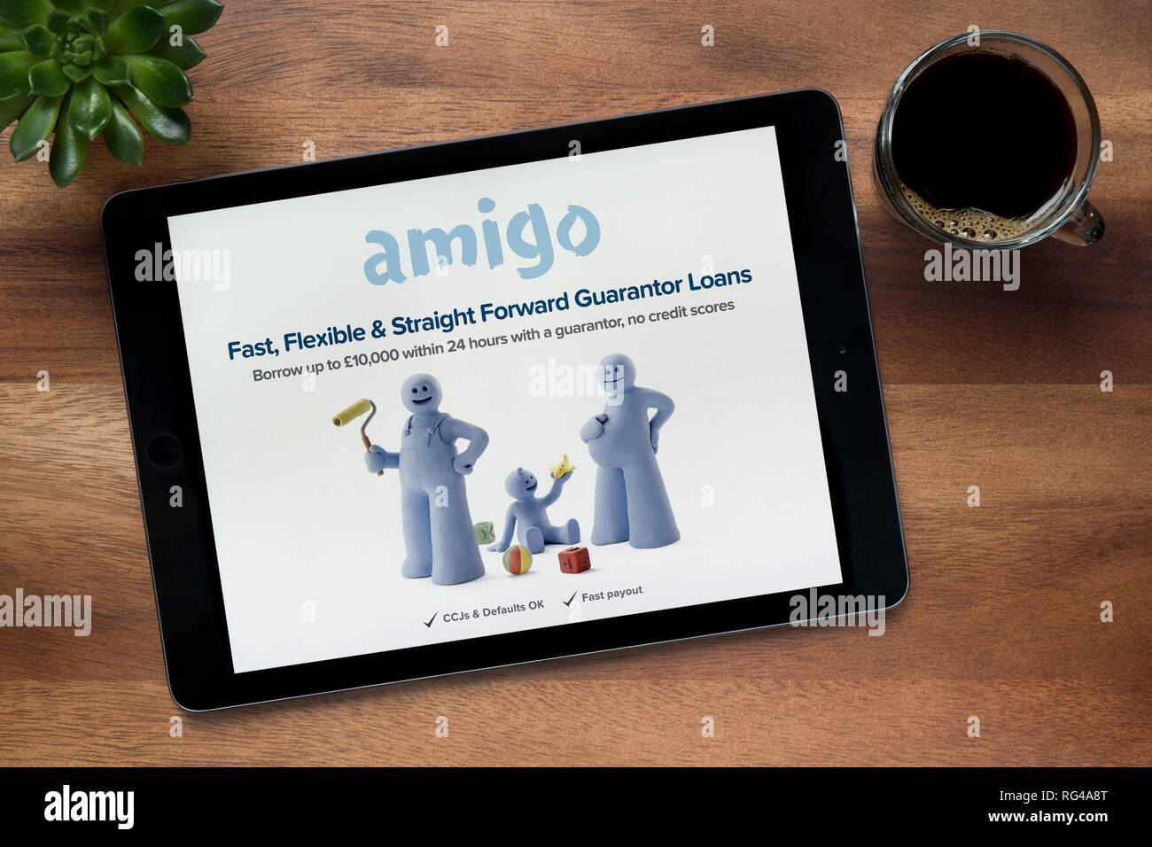 Die Website von Amigo Darlehen ist, auf einem iPad Tablet gesehen, auf einer hölzernen Tisch zusammen mit einem Espresso und einem Haus Anlage (nur redaktionelle Nutzung). Stockfoto