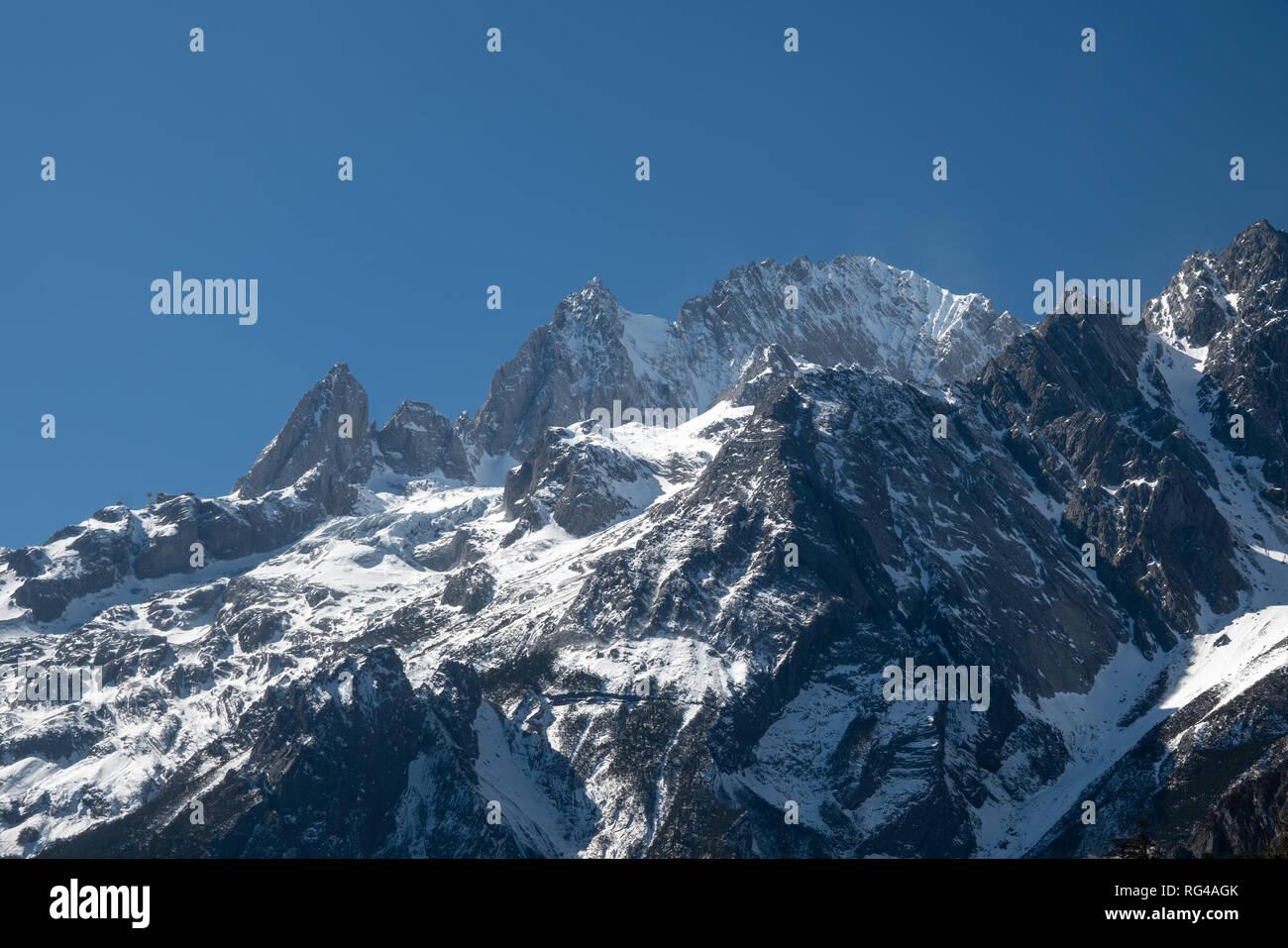 Jade Dragon Snow Mountain in Yulong, Yunnan China. Die schneebedeckten Berge mit felsigen Gipfeln mit Bäumen im Vordergrund, die eine dramatische Stockfoto