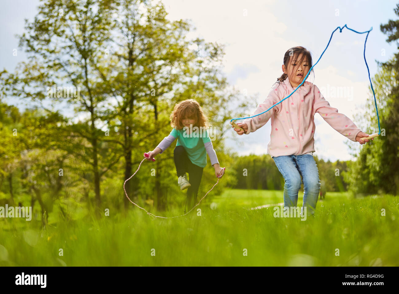 Zwei Mädchen im Seilspringen auf einer Wiese im Park im Sommer Ferien Stockfoto