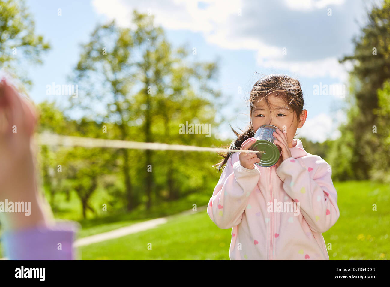 Asiatische Mädchen spricht in einem können Telefon mit Schnur beim Spielen im Park Stockfoto