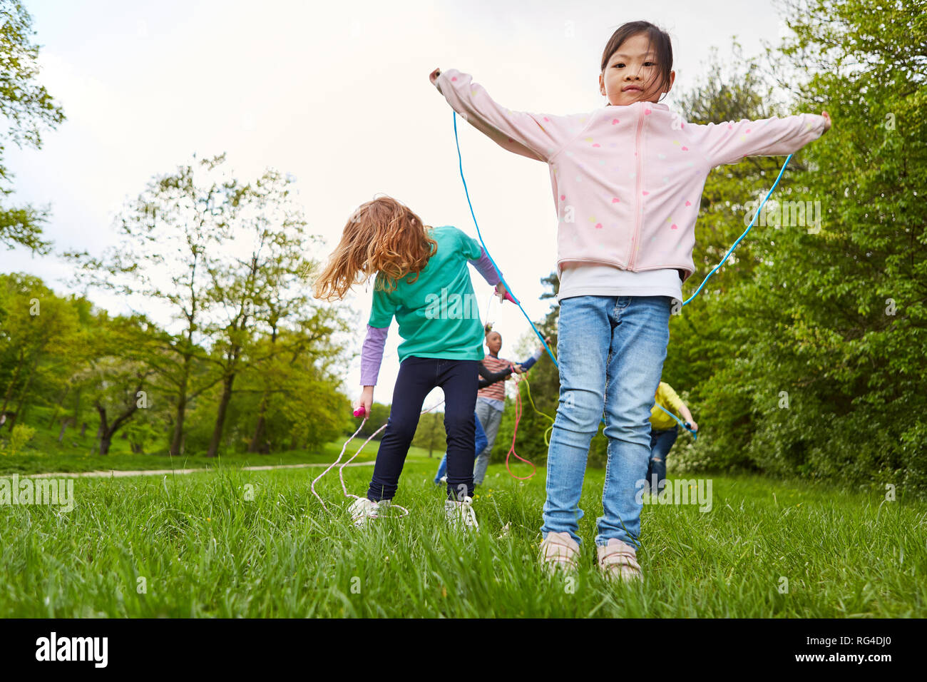 Kinder im Kindergarten zusammen beim springen Seil auf einer Wiese im Sommer Stockfoto