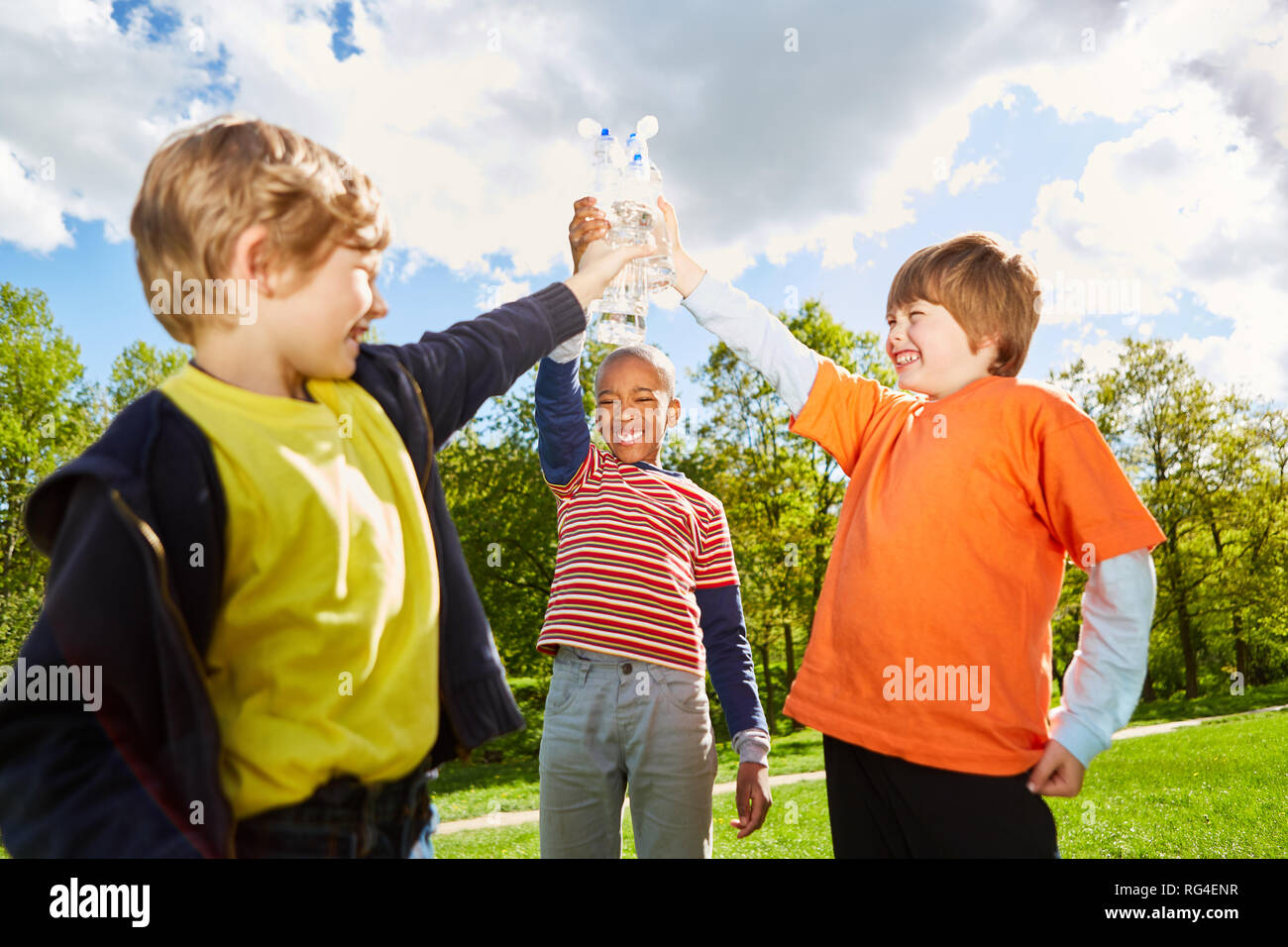 Drei Kinder in den Park starten mit Wasserflaschen als Zeichen ihrer Freundschaft Stockfoto