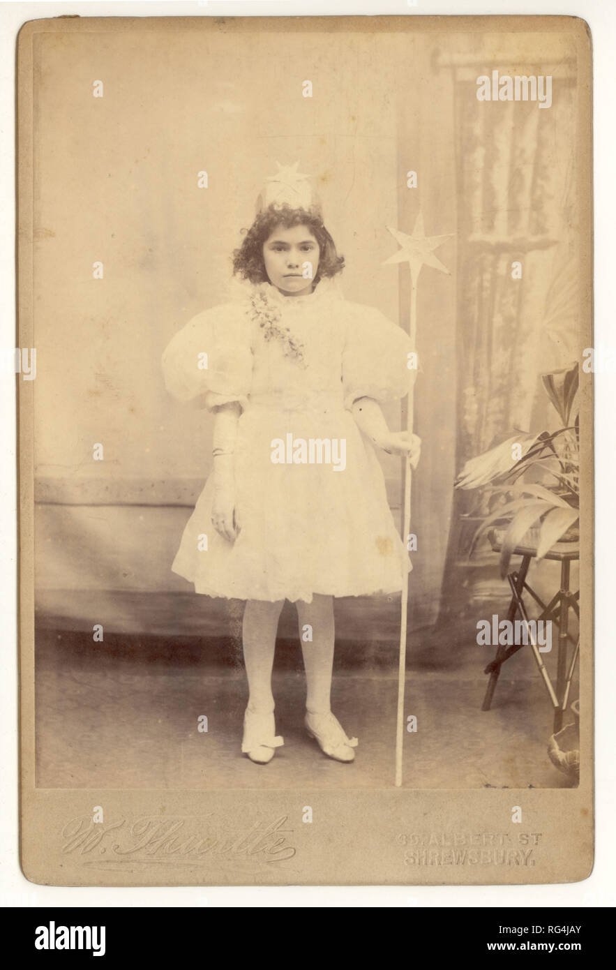 Original leicht verblasst, aber charmant viktorianischen Kabinettkarte Studio-Porträt von jungen Mädchen in weißen Feenkleid oder Königskleid mit einem Zauberstab, trägt eine Krone, für eine Party gekleidet. Fotografiert im W. Hewitts Studio, Shrewsbury, Shropshire, Großbritannien um 1895,1896. Stockfoto