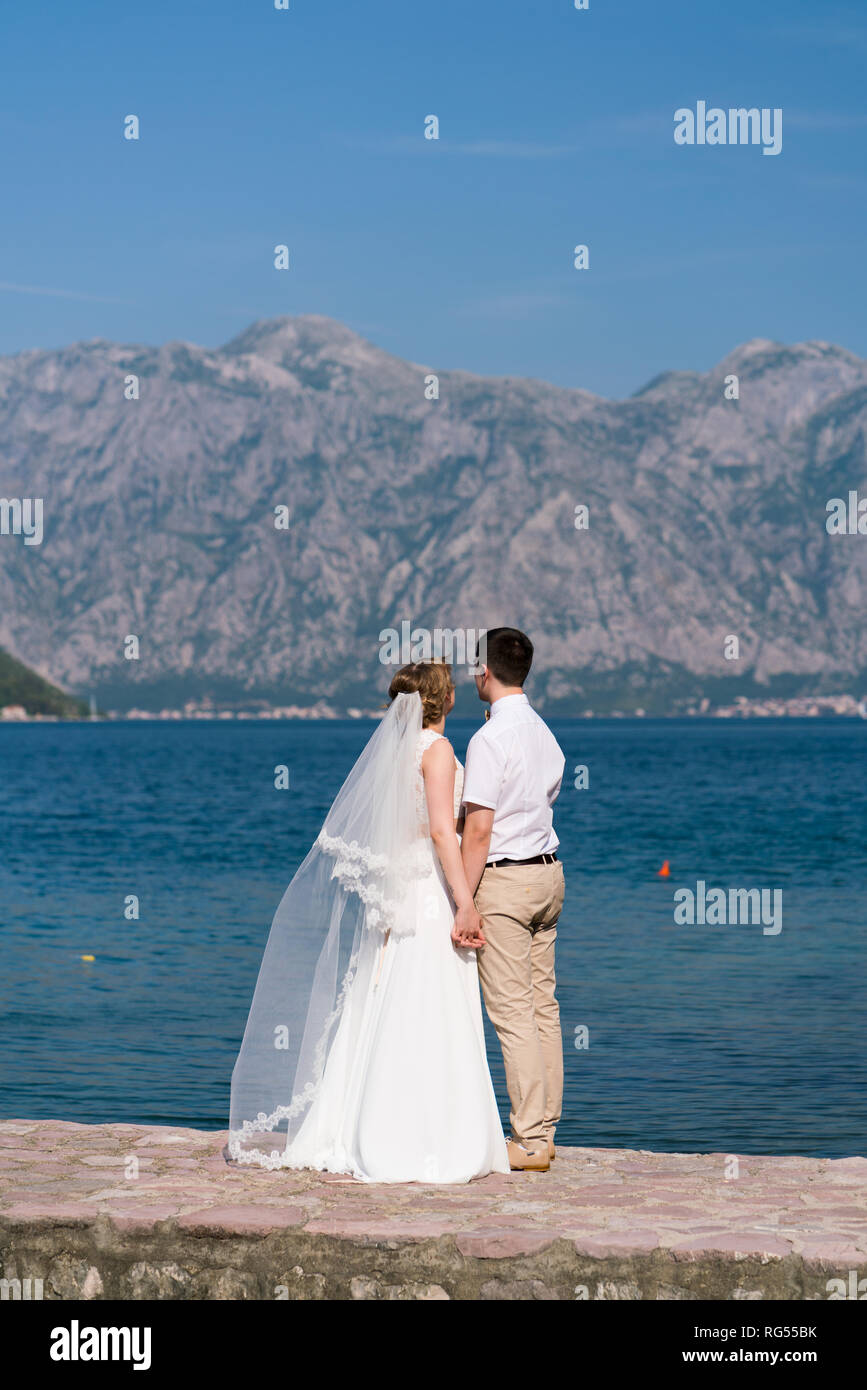 Brautpaar stand auf der Pier an einem sonnigen Tag und an das Meer, das Hände schauen Stockfoto
