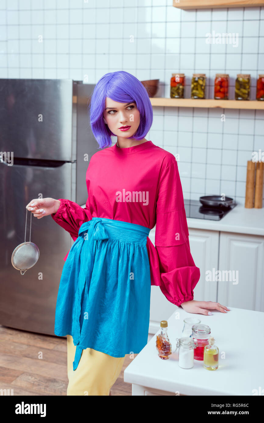 Schöne Hausfrau mit lila Haaren und bunte Kleidung holding Sieb und posiert  in der Küche Stockfotografie - Alamy