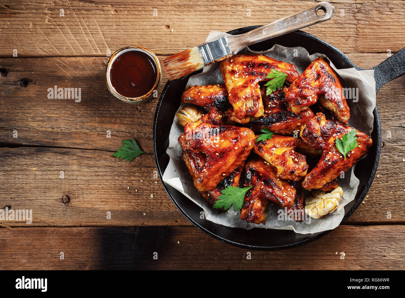 Gebackene Chicken Wings mit Barbecue Sauce in einer gusseisernen Pfanne auf einem alten Holz