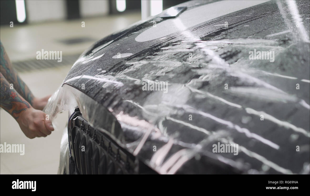 Professionelle Anwendung Schutzfolie mit dem roten Auto. Master Leime einen schützenden Film auf der Motorhaube des Autos Stockfoto