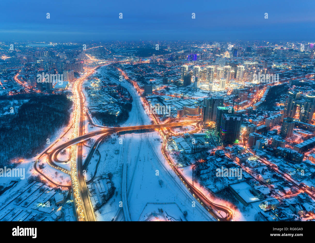 Luftaufnahme der wunderschöne, moderne Stadt in der kalten Nacht im Winter. Blick von oben auf den Verkehr auf Straßen, Gebäude, verschneite Straßen mit Beleuchtung. Skyline. Citys Stockfoto
