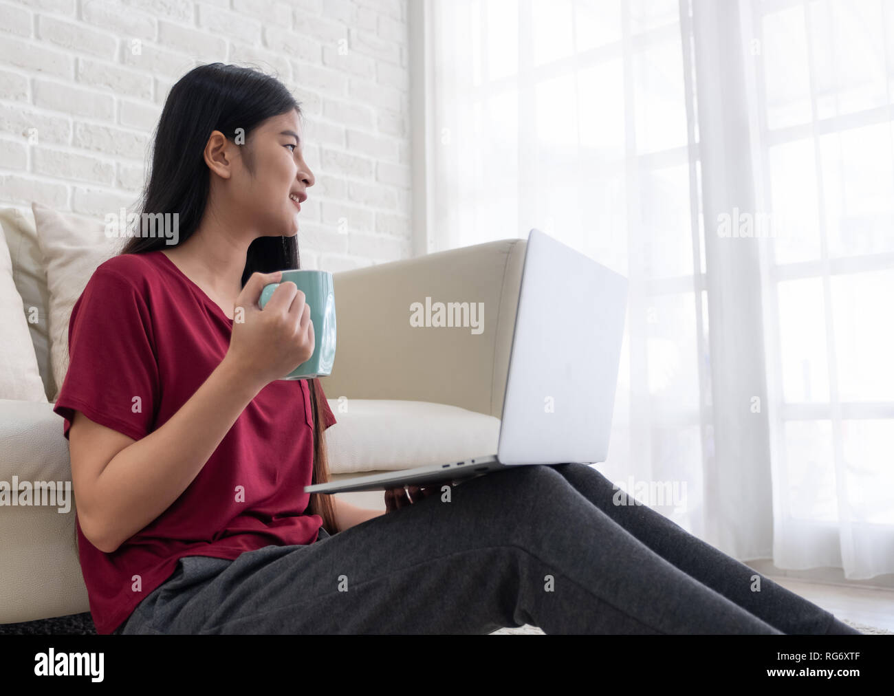 Asiatische Frau Freiberufler Lächeln und Kaffee trinken mit Gefühl entspannen und Suchen aus dem Fenster zu Hause. online arbeiten Lifestyle Stockfoto