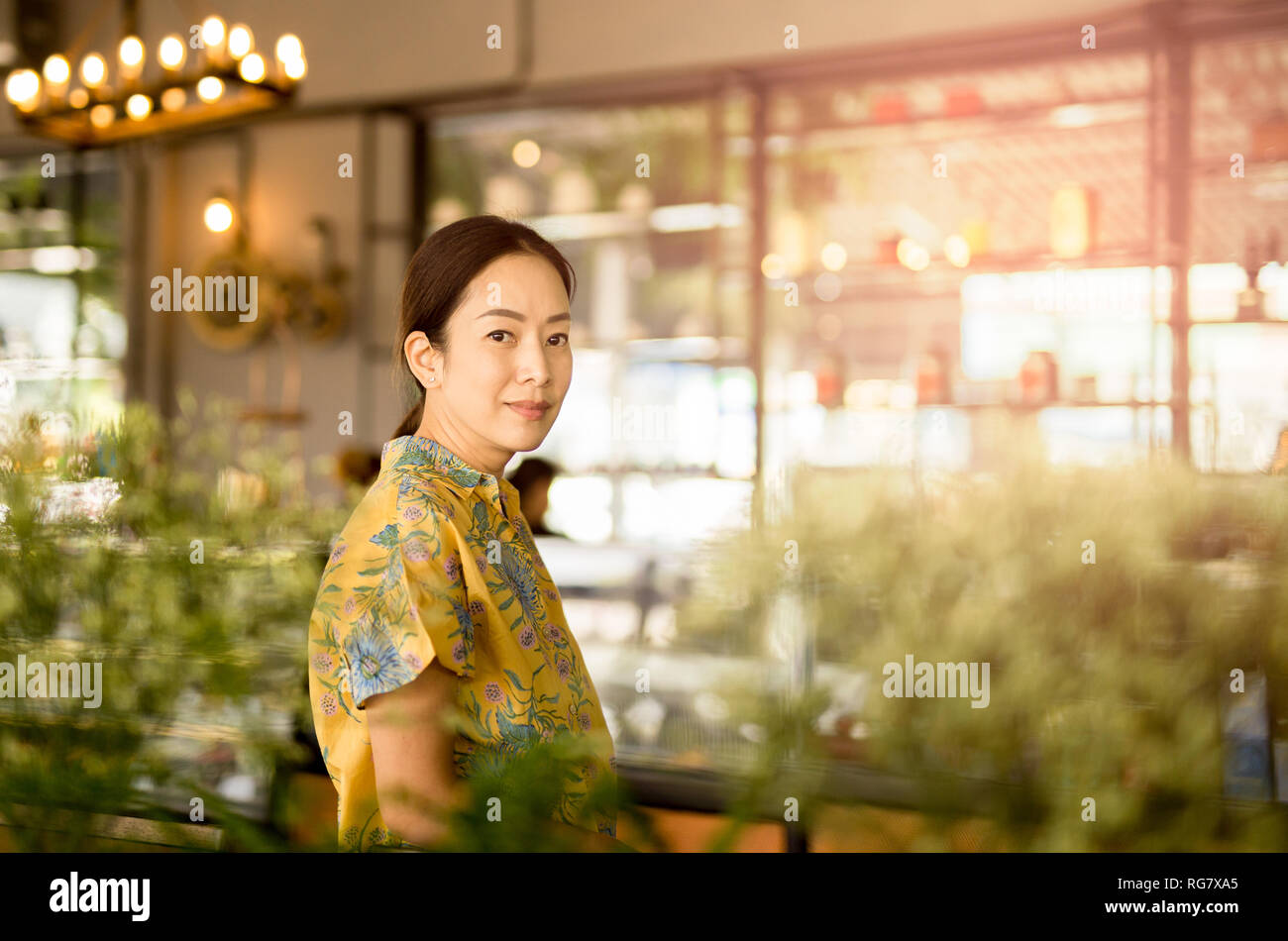 Schöne asiatische Frau mittleren Alters an der Kamera im Coffee Shop. Stockfoto