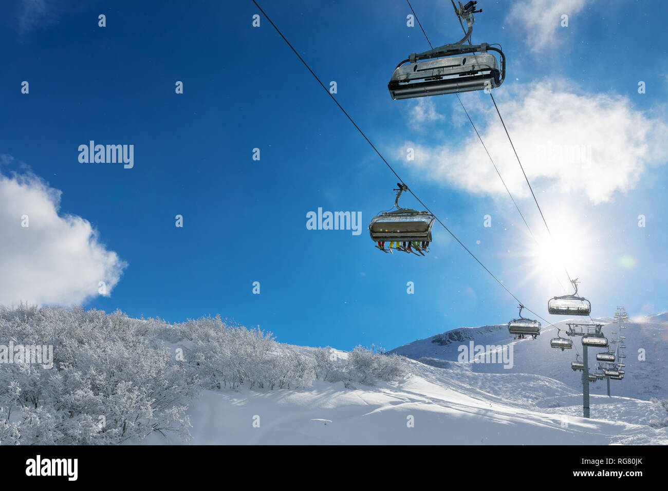 Skifahrer in einem Skilift in Snowy Mountains gegen den blauen sonnigen Himmel Stockfoto