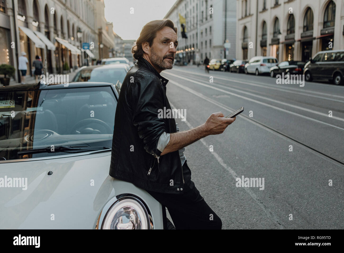 Reifer Mann lehnte sich auf dem Auto, Smartphone, München, Bayern, Deutschland Stockfoto