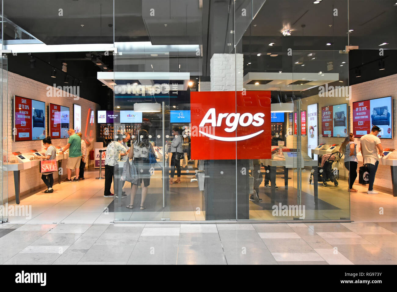 Käufer hinter Glas Gebäude shop Fenster vorne im Argos Katalog shopping Store in Westfield Mall in Stratford City Newham East London England Großbritannien Stockfoto