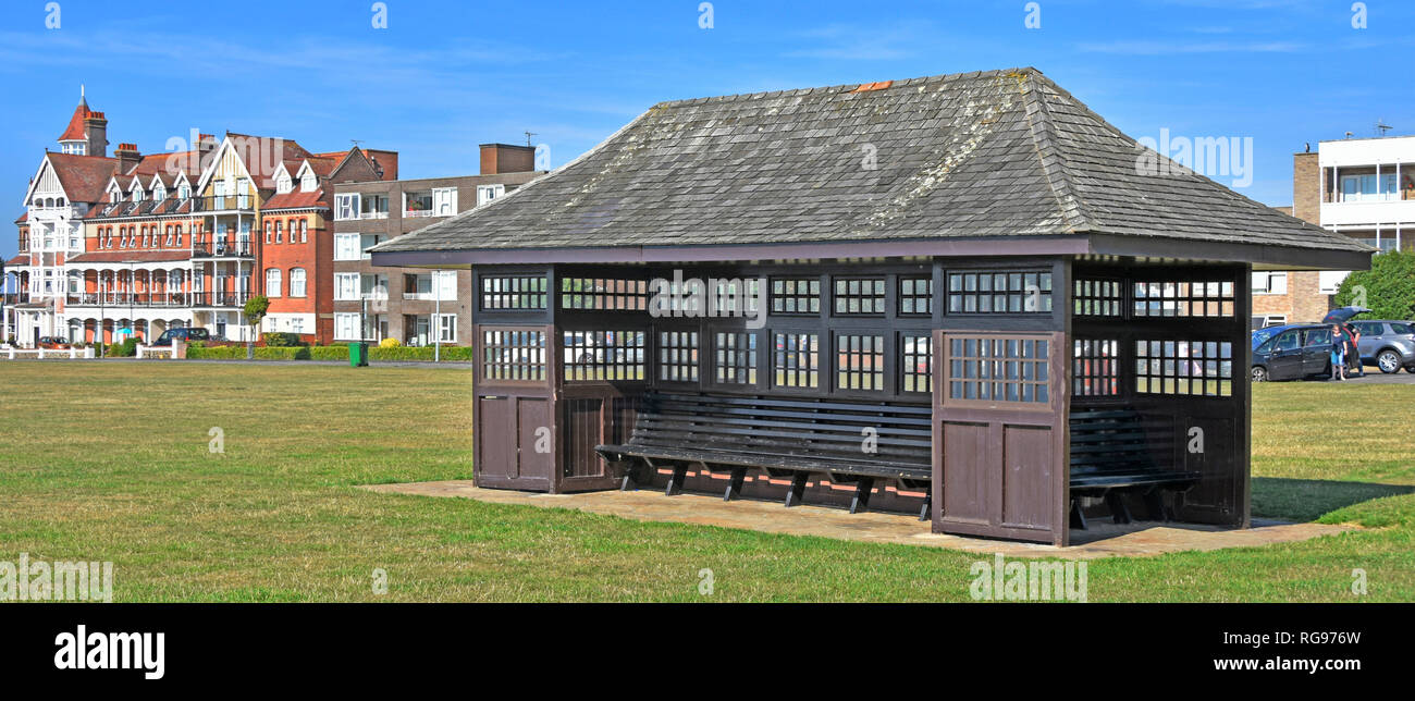 Traditionelle Holz Tierheim & Sitze im Urlaub Seebad Promenade mit viktorianischen Apartment rotes Ziegelgebäude über Frinton-on-Sea Essex UK Stockfoto