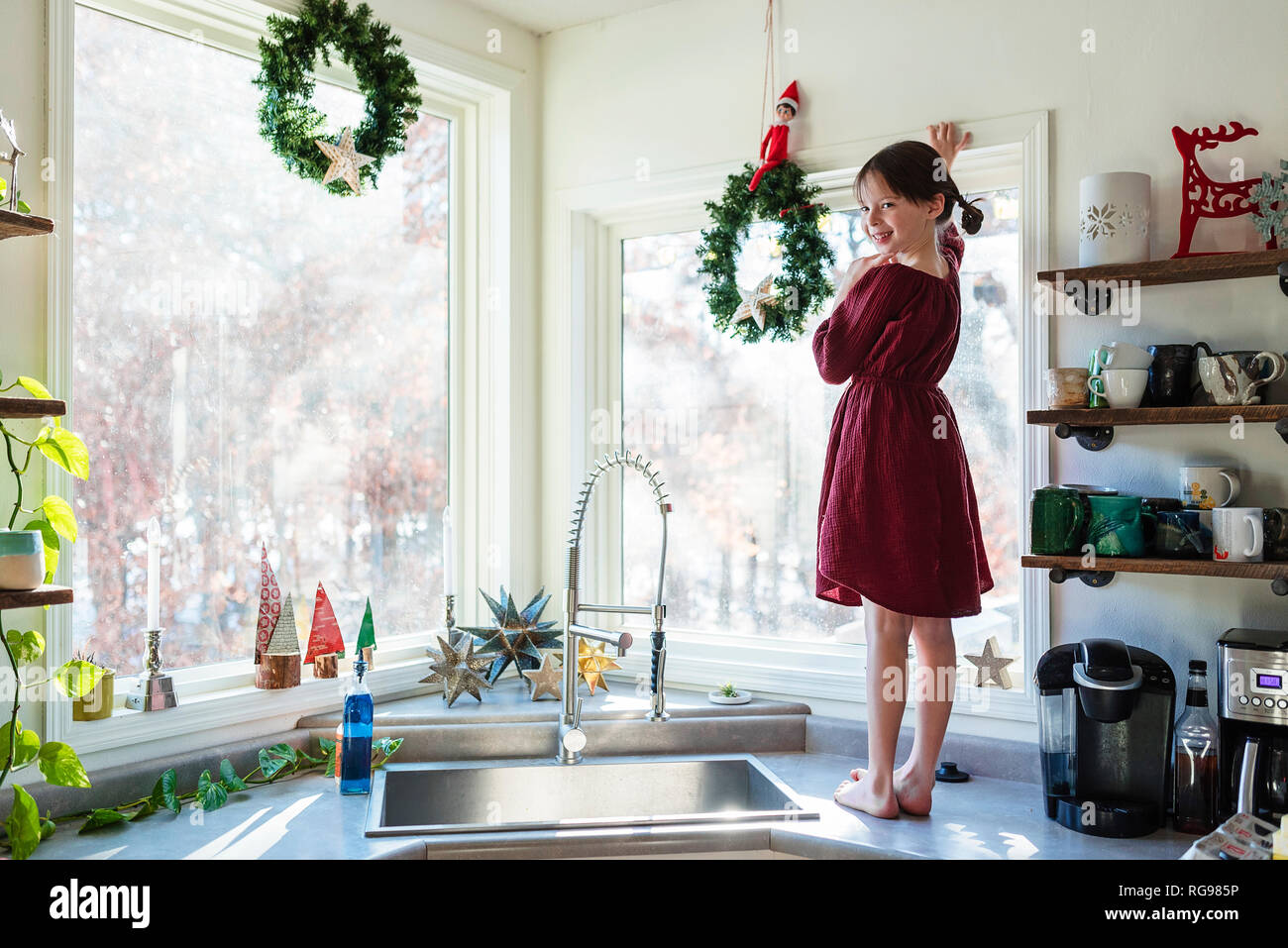 Lächelnde Mädchen stehen auf einer Küchenarbeitsplatte herauf Weihnachtsdekorationen Stockfoto
