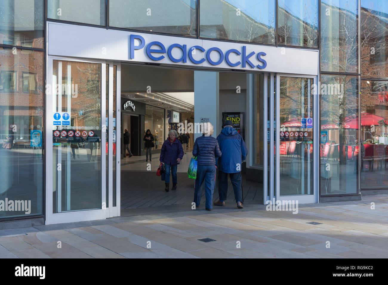Menschen (Shopper) gehen in die und aus der Pfauen Shopping Center, ein Einkaufszentrum in Woking, Surrey, Großbritannien Stockfoto