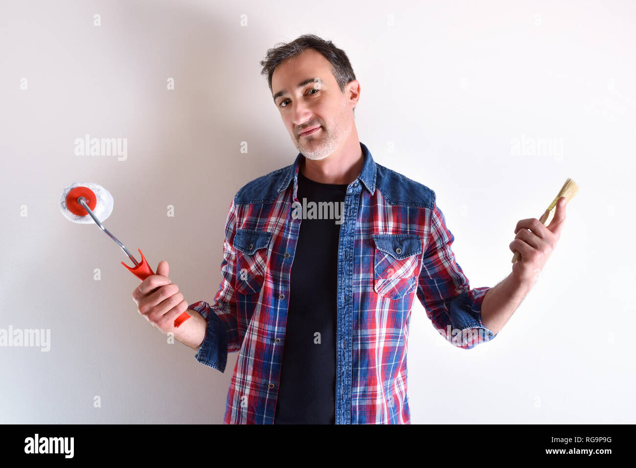 Mann mit Rolle und Pinsel und weiße Wand hinter sich. Diy home Konzept. Vorderansicht. Horizontale Komposition. Stockfoto