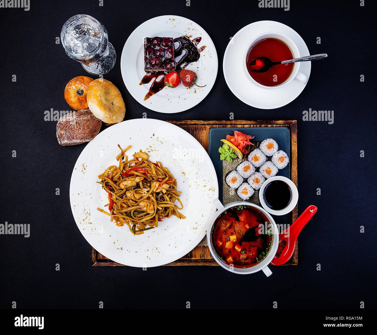 Asiatische Lebensmittel. Gebratene Nudeln mit Huhn, Misosuppe, Sushi mit Lachs, Tasse Kaffee und Kuchen. Stockfoto
