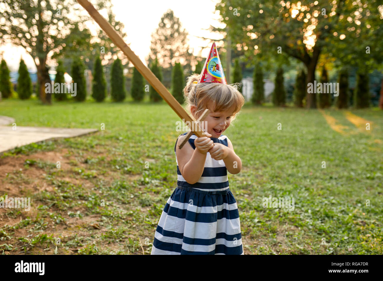 Glückliche kleine Mädchen mit Party Hut und Holding Holzschwert in Garten Stockfoto