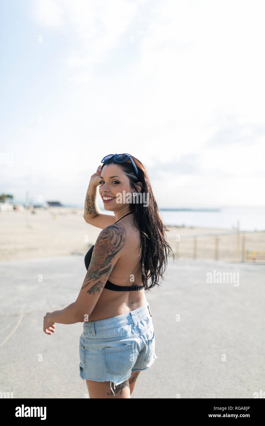 Portrait von lächelnden jungen Frau mit Nasen Piercing und Tattoos auf dem Weg zum Strand Stockfoto
