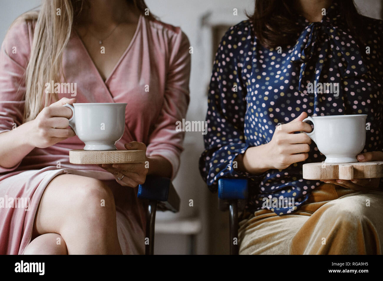 Zwei Frauen sitzen Seite an Seite mit Holzbrettern mit weißer Tee Tassen, Teilansicht Stockfoto