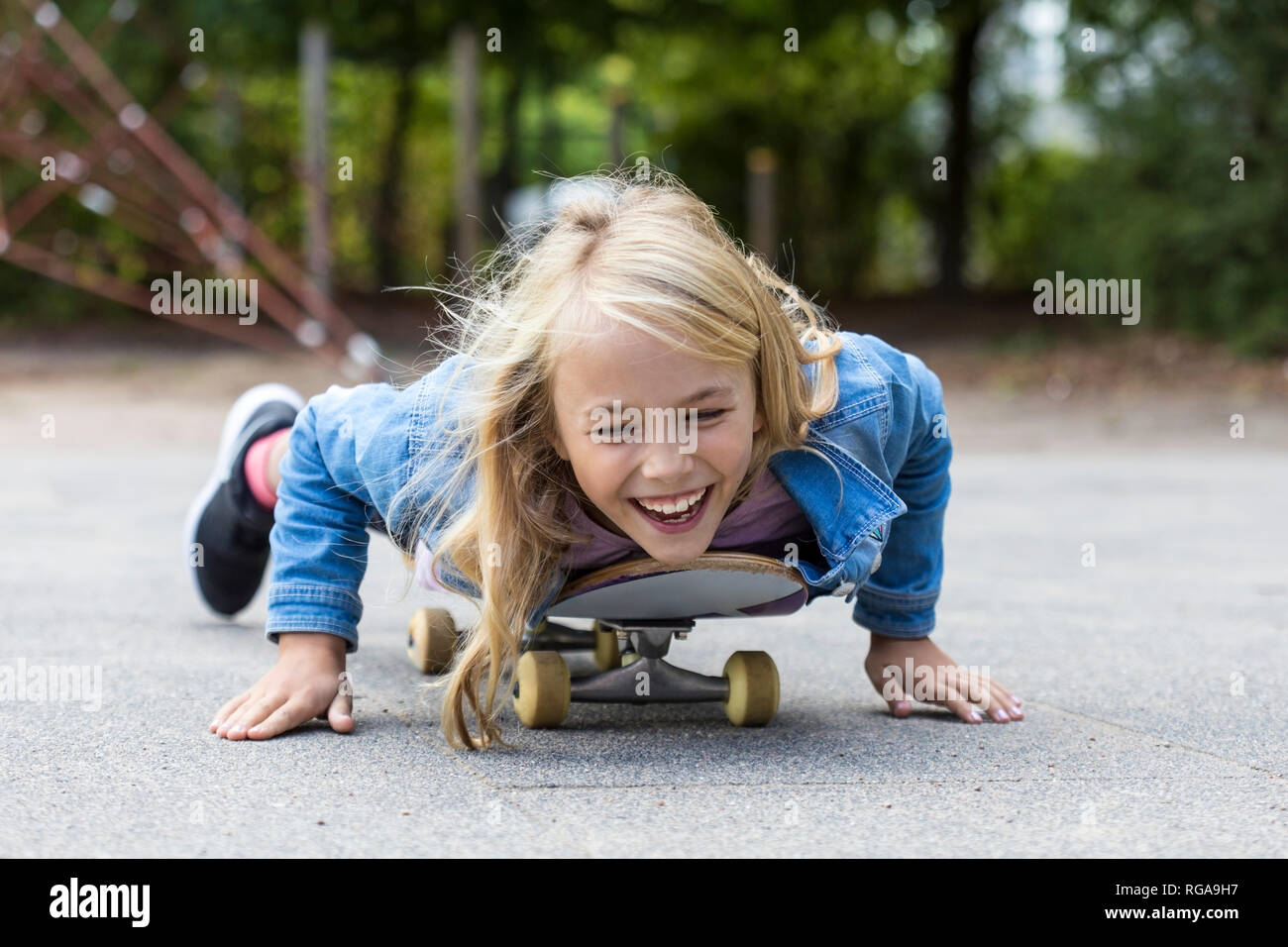 Portrait von Lachen blonde Mädchen liegt auf dem Skateboard im Freien Stockfoto