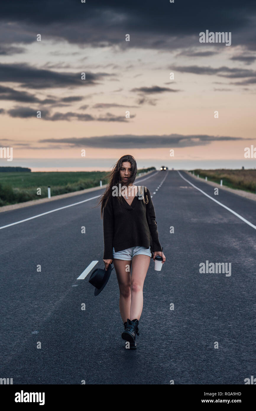 Portrait von Per Anhalter junge Frau mit Rucksack und Getränke gehen auf Spur am Abend dämmerung Stockfoto