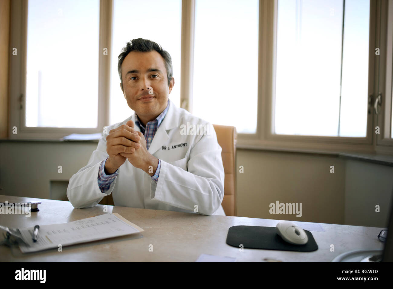 Porträt eines mittleren Alters Arzt an seinem Schreibtisch sitzen. Stockfoto