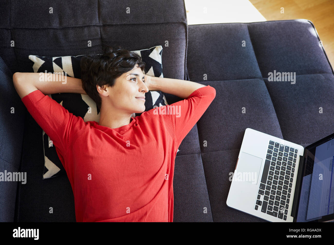 Liegende Frau auf der Couch zu Hause neben Laptop Stockfoto