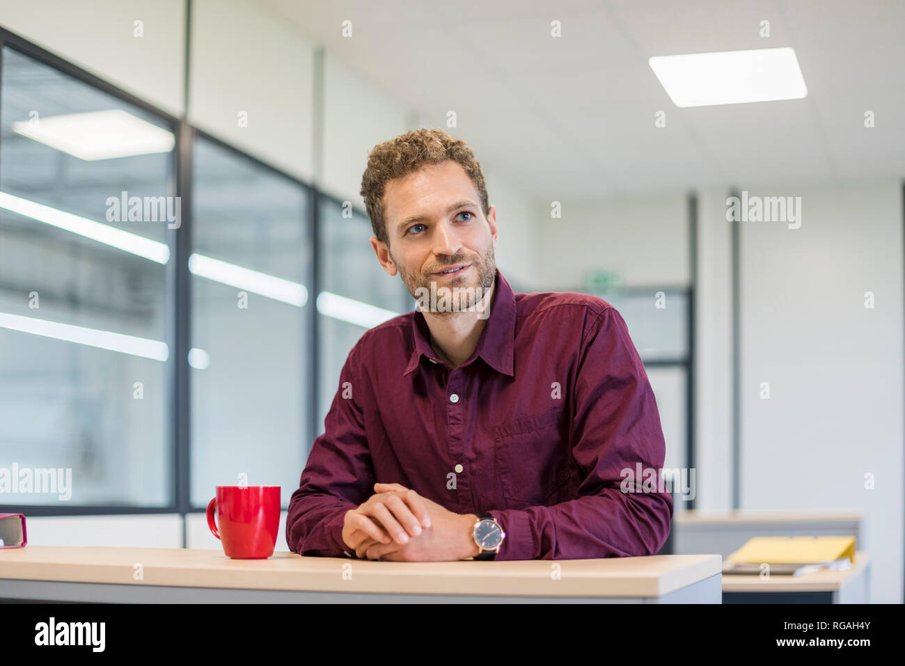 Im Büro am Schreibtisch mit roten Kaffeetasse sitzend Stockfoto