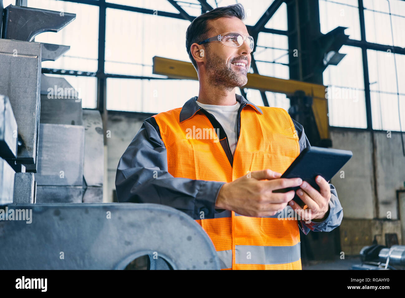 Lächelnder Mann mit Tablet Tragen von Arbeitskleidung in der Factory Stockfoto