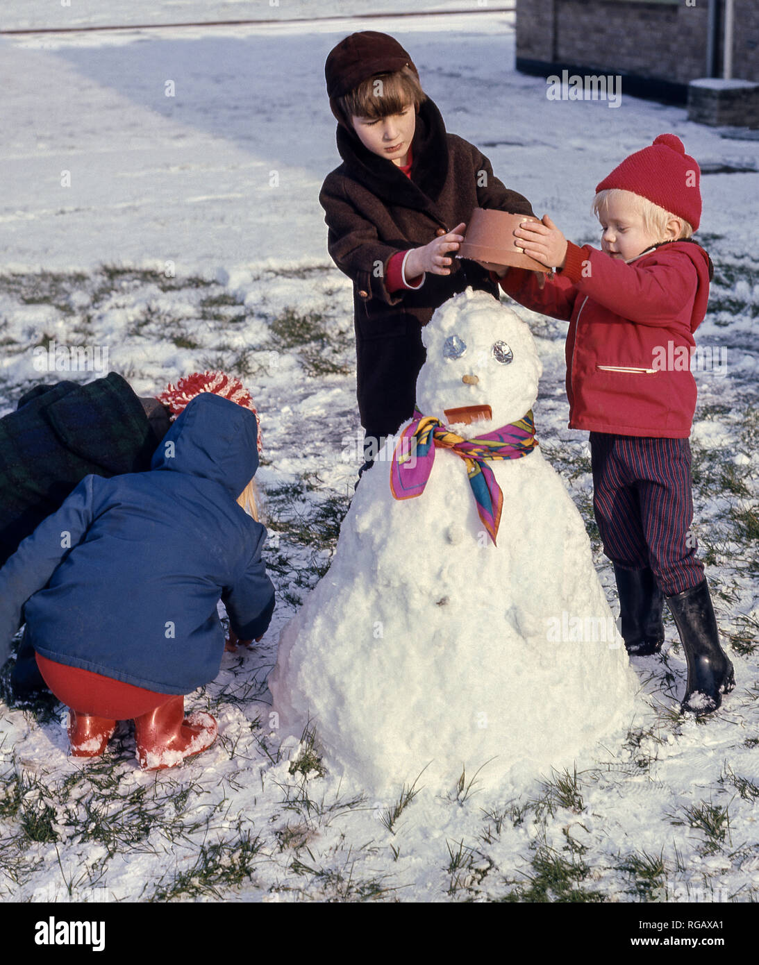 Vier junge Kinder den letzten Schliff an einen Schneemann. Stockfoto