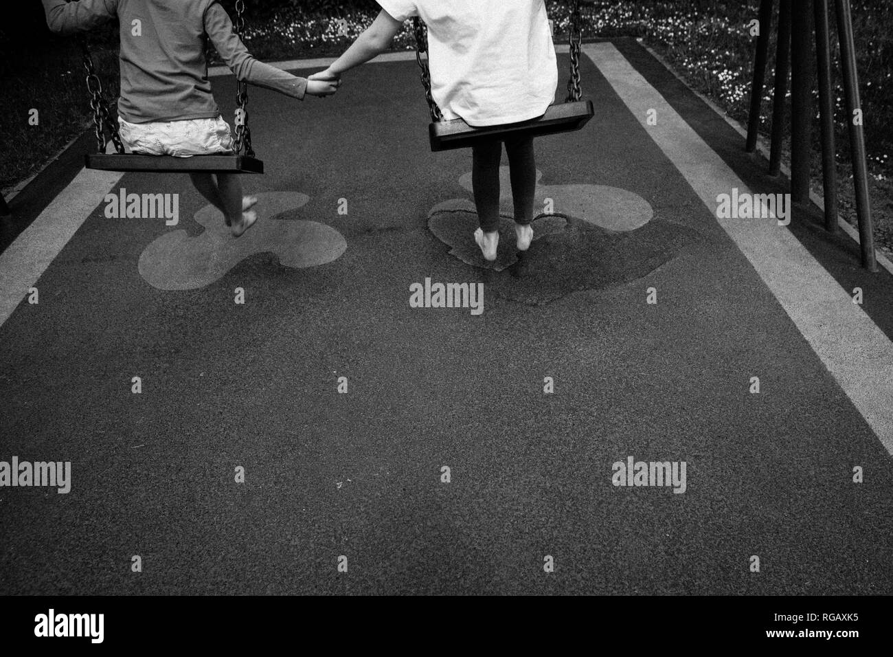 Schwarz-weiß Foto von zwei Latina Mädchen, auf Schaukeln in einem Park auf einem Spielplatz halten sich an den Händen Stockfoto