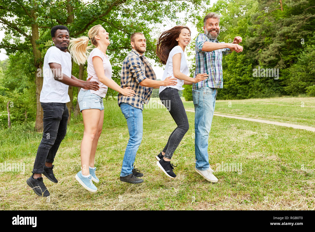 Happy multikulturelle Gruppe hopping auf einer Wiese am Teambuilding Event Stockfoto