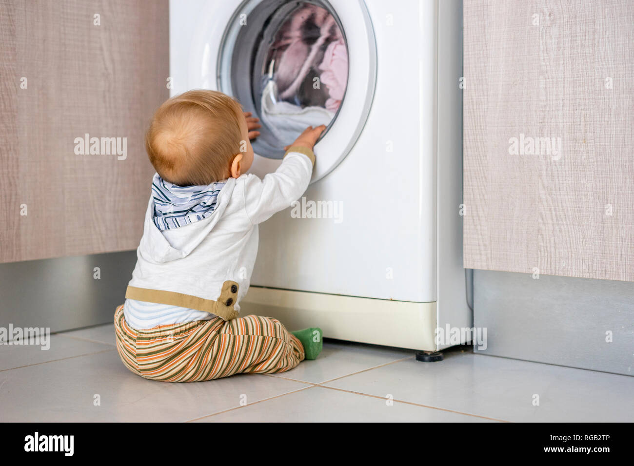 Baby Boy in den Zyklen der Waschmaschine Wäsche interessiert Stockfoto