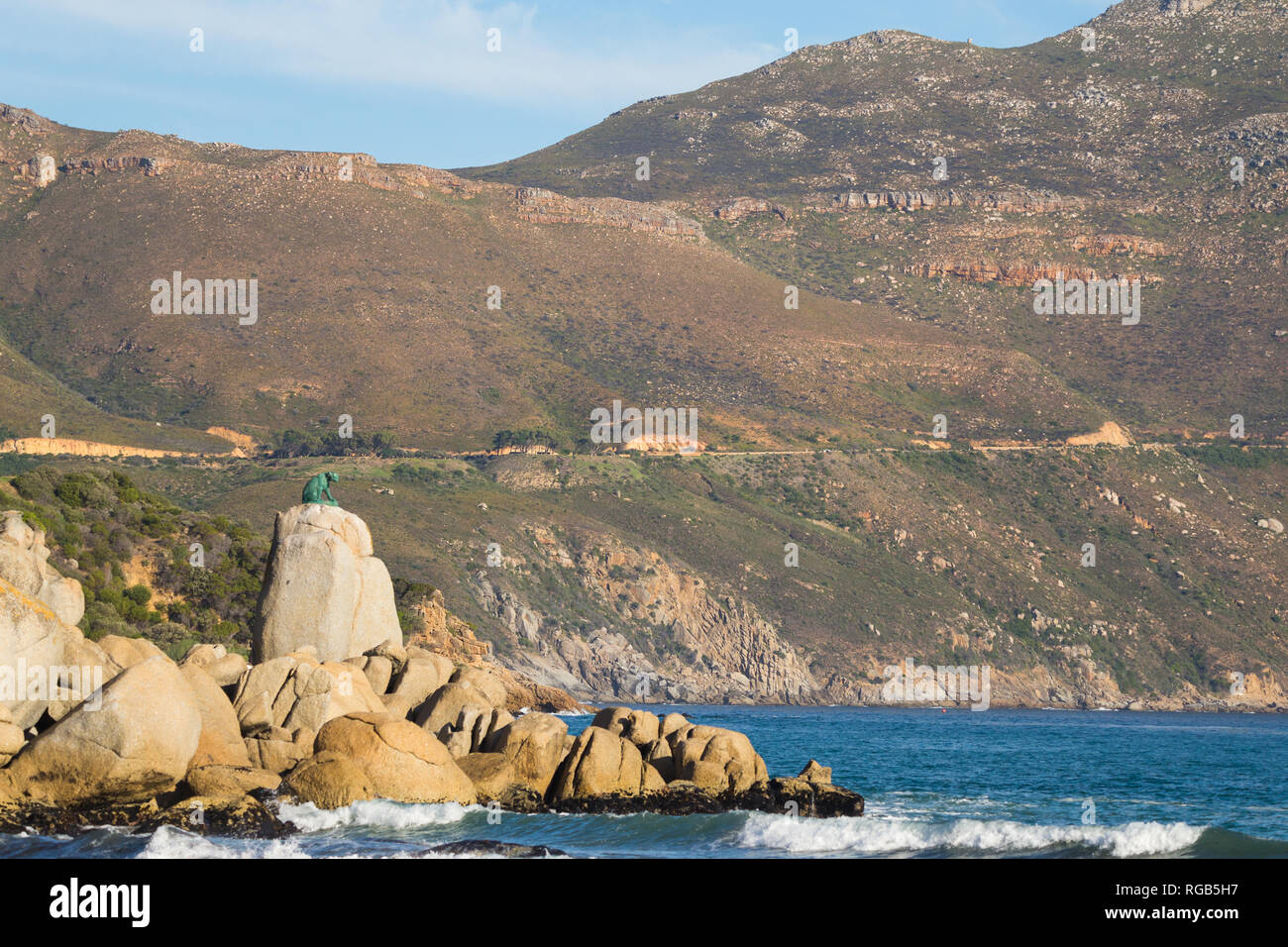 Chapmans Peak Drive entlang der Berg hinter die Bronzestatue des Leopard auf den Felsen wie von Hout Bay Strand an einem sonnigen Herbstnachmittag gesehen Stockfoto