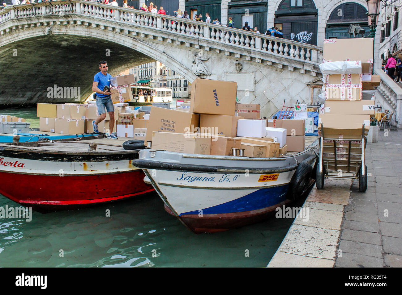 Italienische Arbeiter ist die Entladung von Paketen von einem Boot aus Lieferung von DHL an der Rialtobrücke in Venedig, Italien Stockfoto
