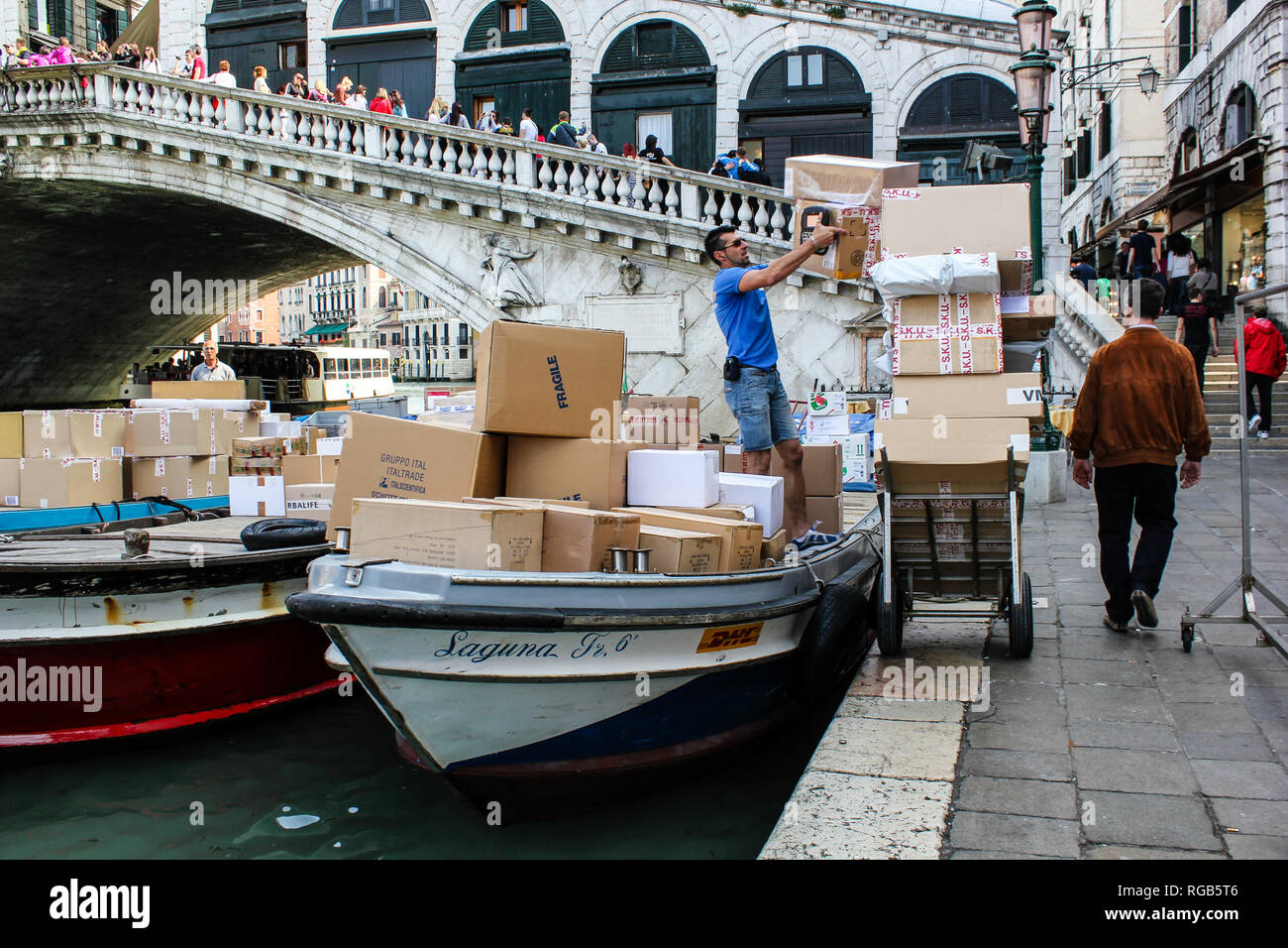 Italienische Arbeiter ist die Entladung von Paketen von einem Boot aus Lieferung von DHL an der Rialtobrücke in Venedig, Italien Stockfoto