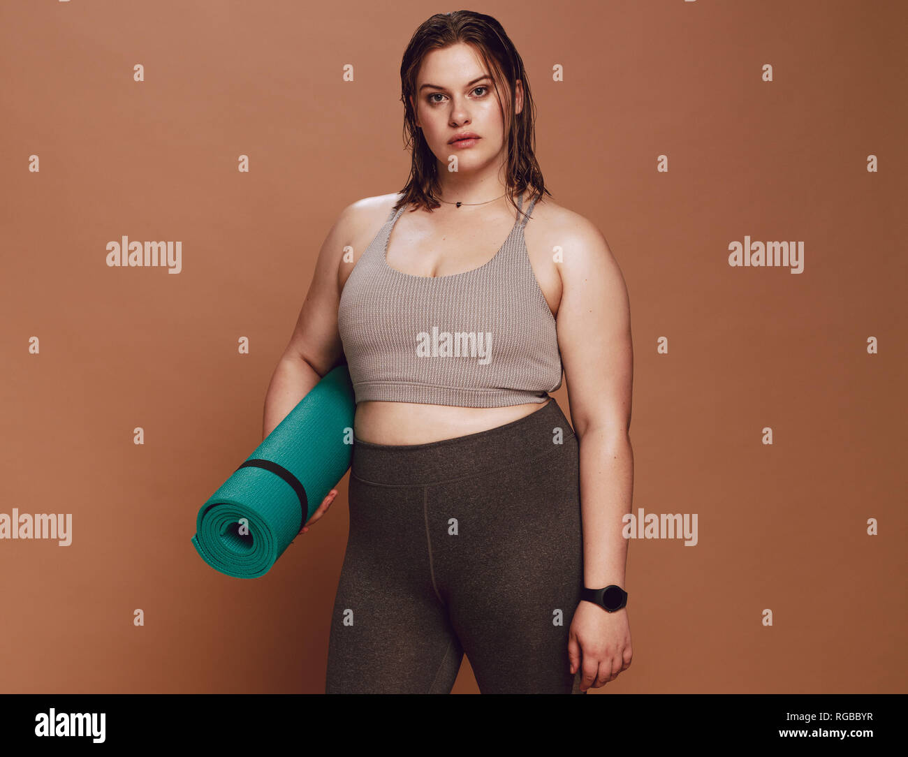 Gesunde junge Frau mit Sportbekleidung mit Yoga Matte gegen braunen Hintergrund. Stockfoto