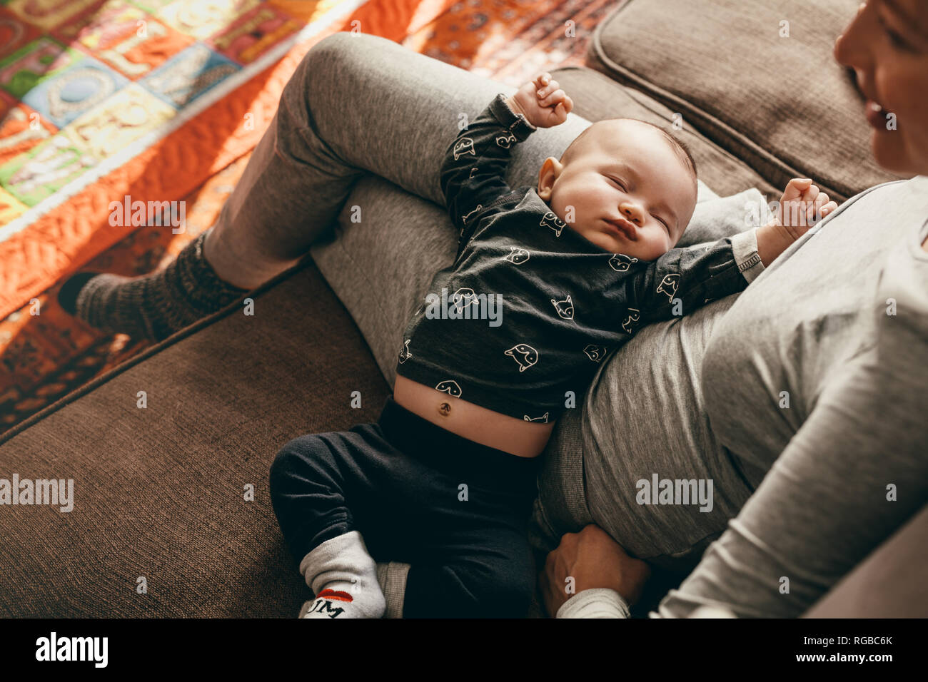 Baby in einen tiefen Schlaf in den Schoß seiner Mutter zu Hause. Mutter sitzt auf der Couch, mit ihrem Baby schlafen in ihren Schoß. Stockfoto