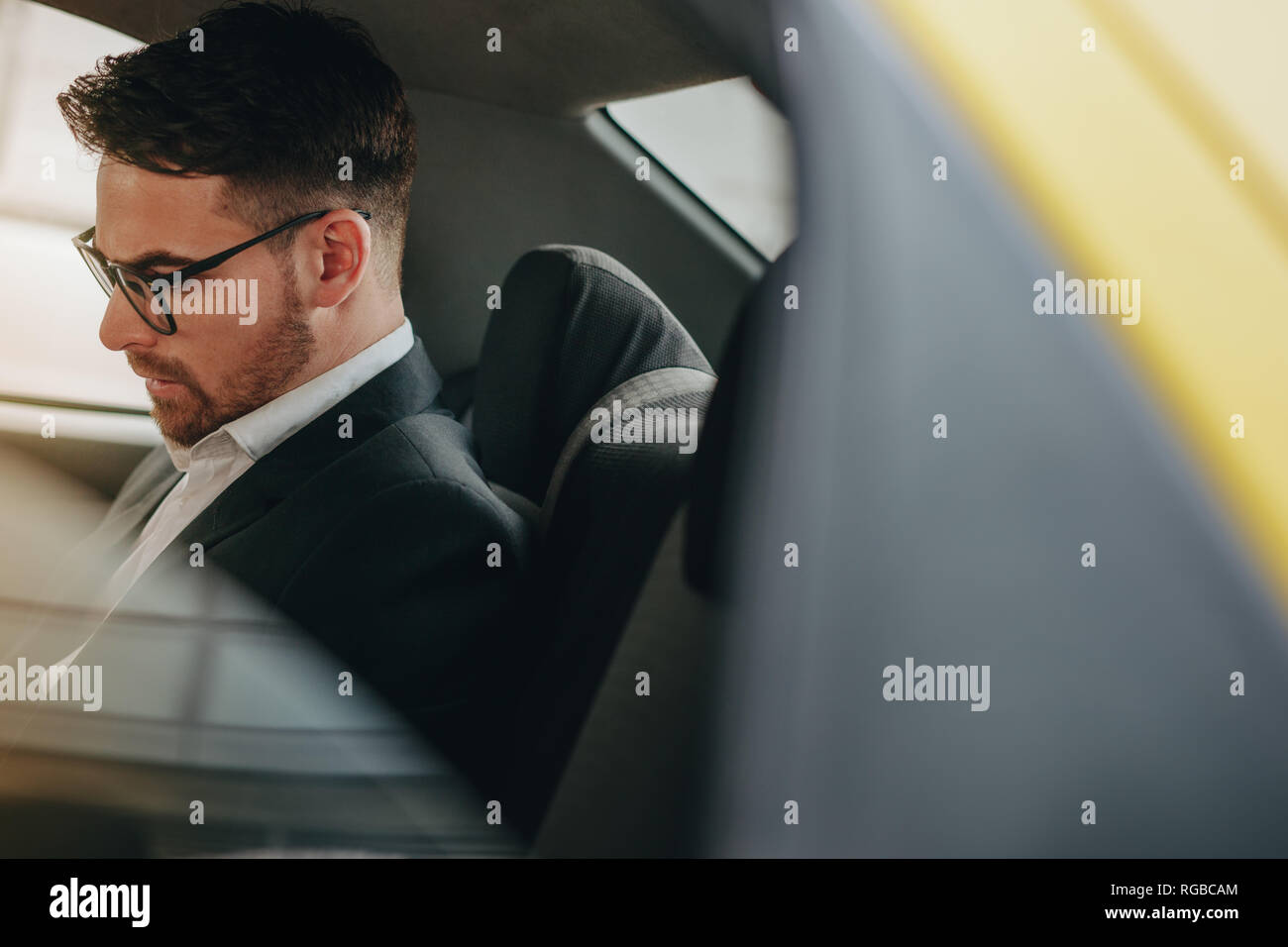 Business Person tragen Brillen sitzen auf dem Rücksitz eines Autos Büro gehen. Seitenansicht eines Kaufmanns im Auto sitzen auf der Suche beschäftigt. Stockfoto
