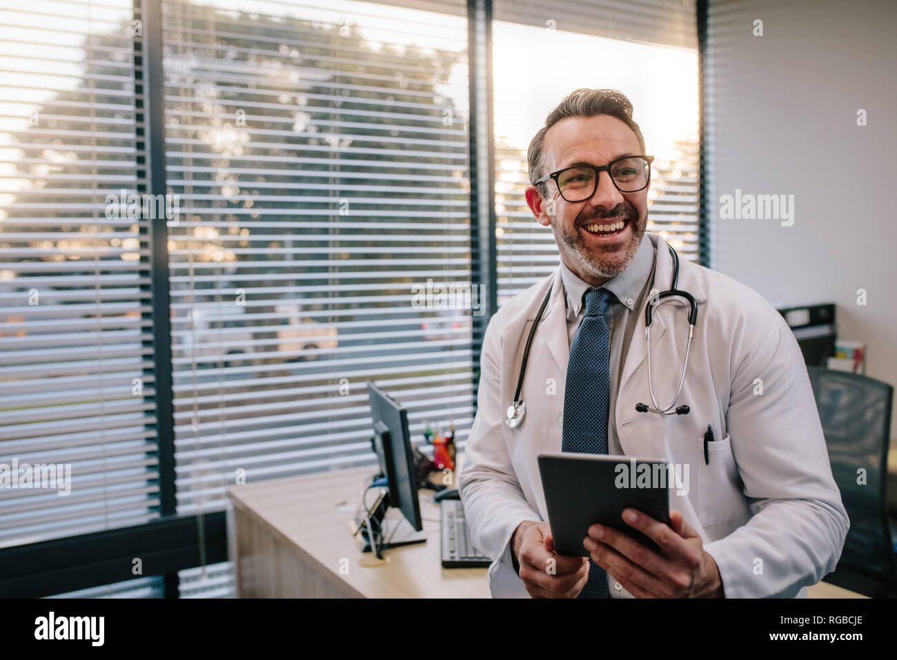 Lächelnd reife männlicher Arzt mit digitalen Tablet in seinem Büro. Freundlichen Arzt mit Tablet-PC in der Klinik. Stockfoto