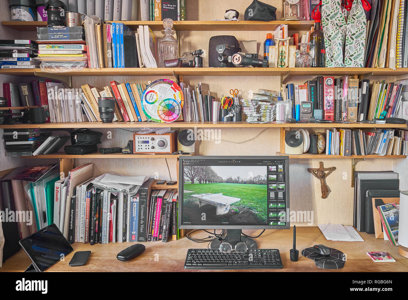 Überfüllte Mischung aus Büchern und anderen Geräten, einschließlich Computer Monitor in ein organisiertes Chaos auf Bücherregale und einen Tisch im Arbeitszimmer. Stockfoto
