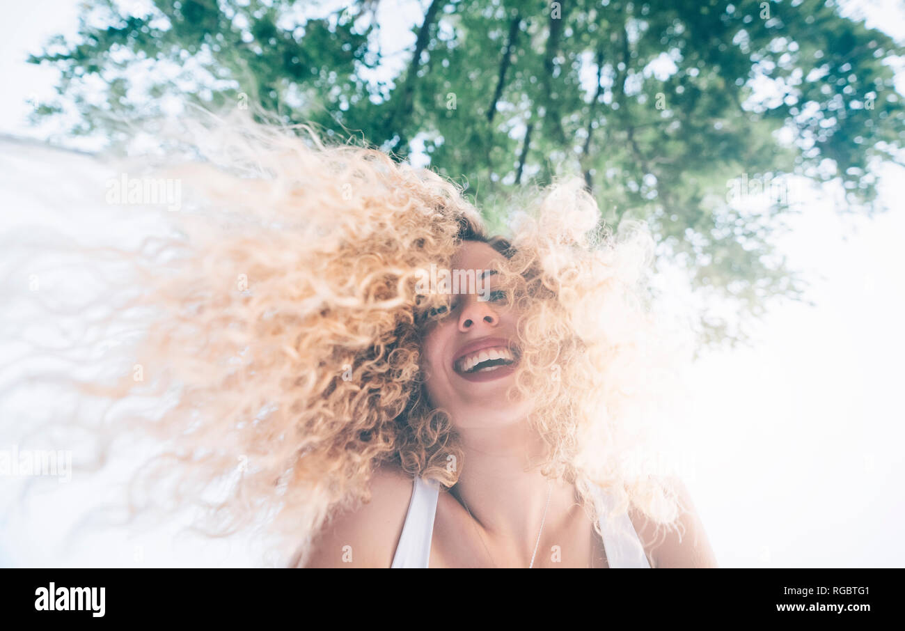 Porträt der glückliche junge Frau mit blonden Löckchen an der Hintergrundbeleuchtung Stockfoto