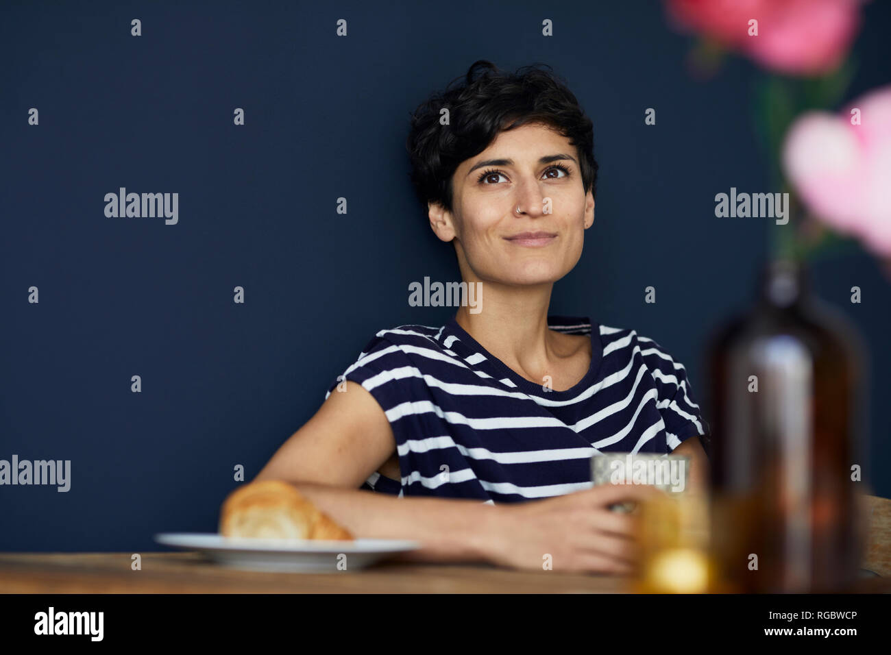 Portrait von lächelnden Frau, die zu Hause an den hölzernen Tisch sitzen Stockfoto