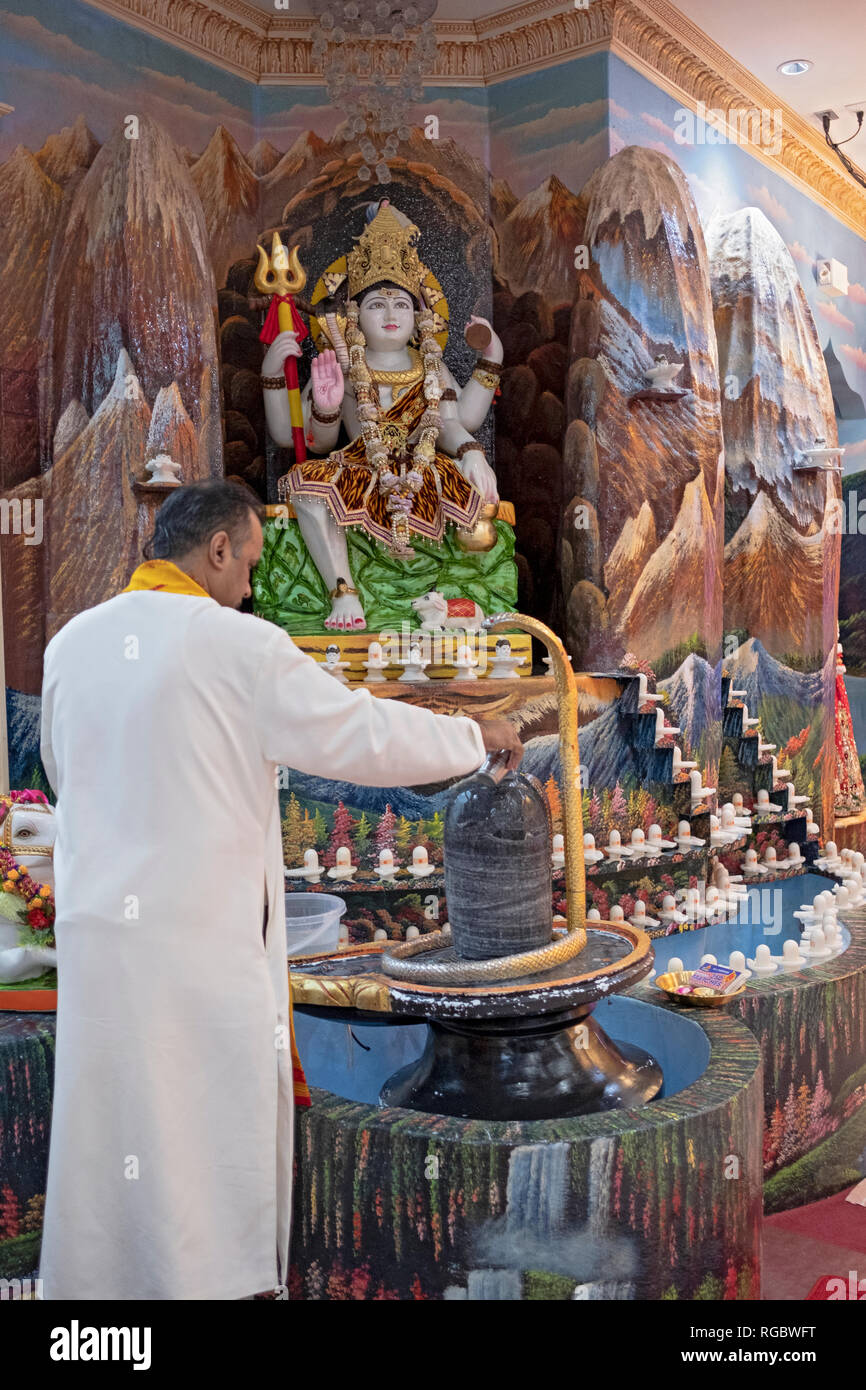 Ein hinduistischer Priester betend und meditierend vor einem Lingam und Abbild der Göttin Shiva. An einem Tempel in South Richmond Hill, Queens, New York. Stockfoto