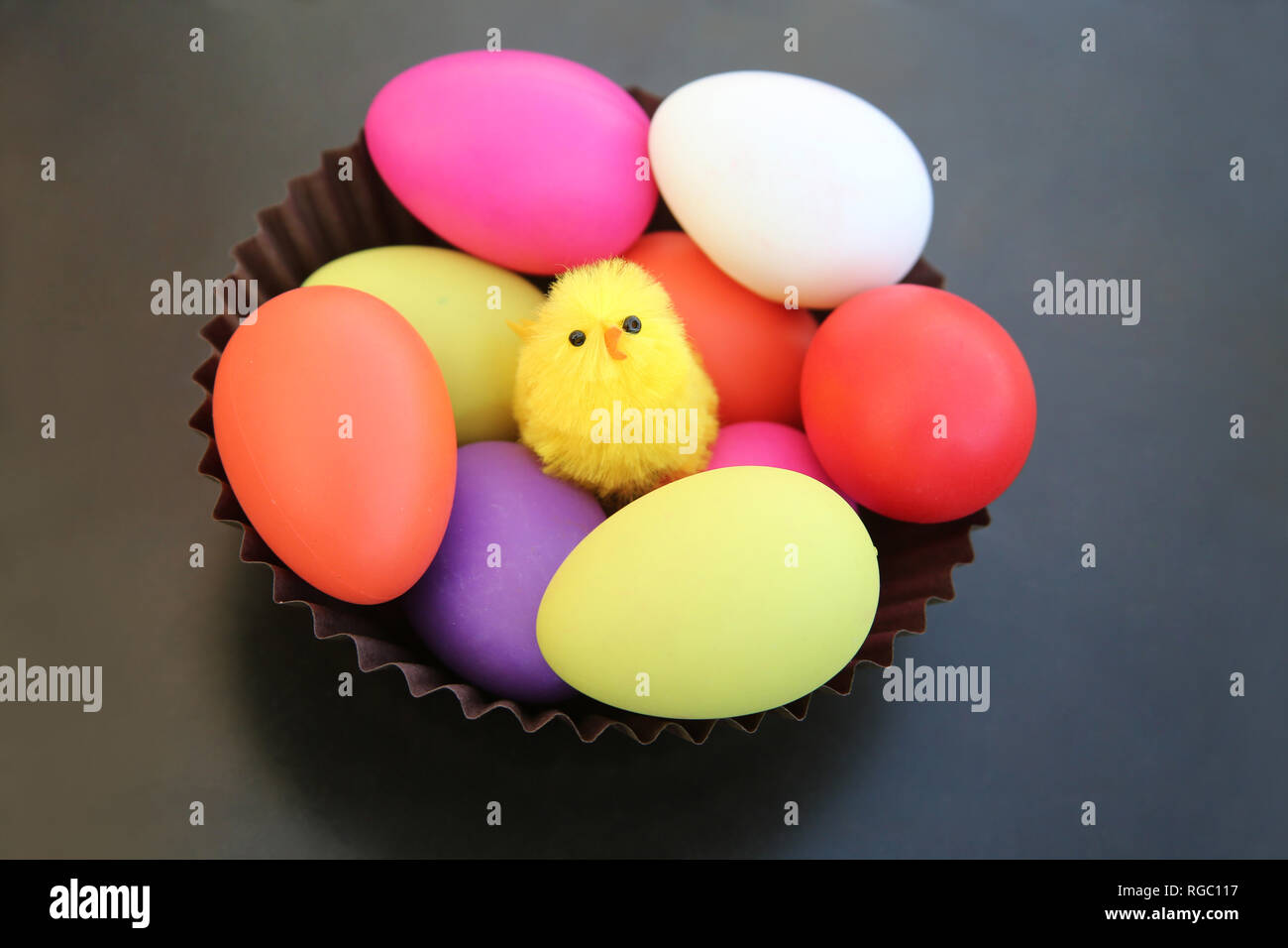 Gelbe Küken sitzend mit bunten Ostereier in einer braunen Korb gegen einen dunklen grauen Hintergrund. Stockfoto