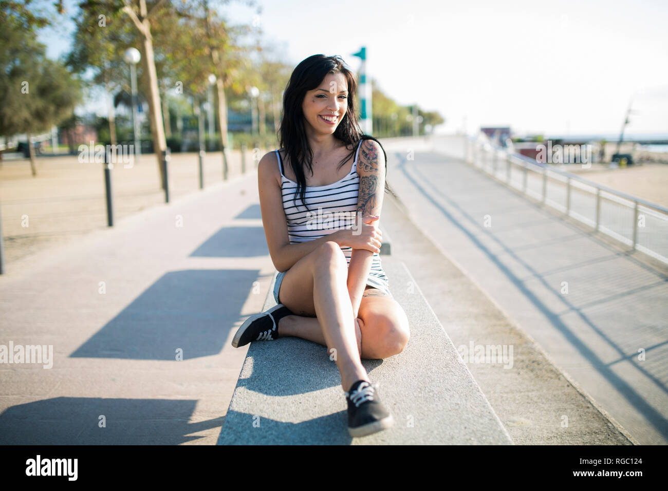 Lächelnd tätowierte junge Frau entspannend auf der Werkbank Stockfoto