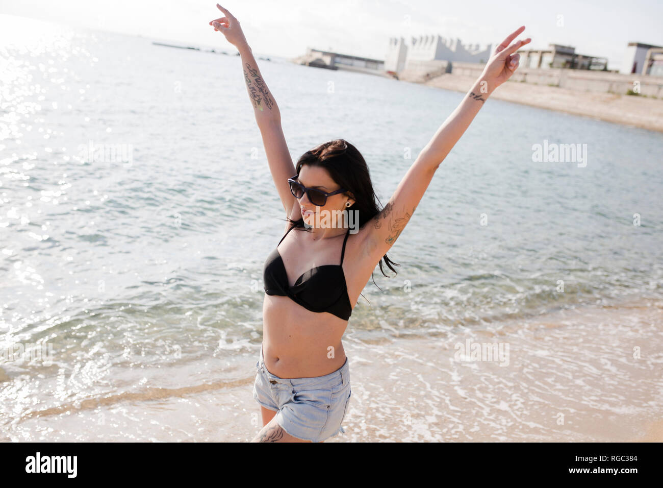 Glückliche junge Frau zu Fuß an der Küste mit erhobenen Armen Stockfoto